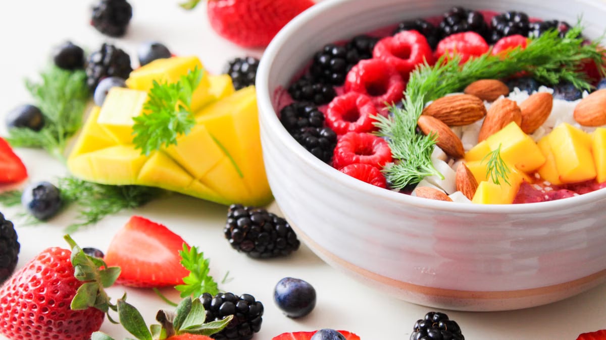 A vibrant bowl filled with fresh berries, mango, almonds, and herbs, perfect for a healthy snack or breakfast.